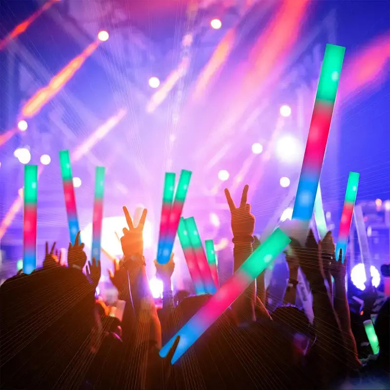 LED foamstick, Een groep mensen houdt kleurrijke LED foamsticks omhoog tijdens een concert, met levendige kleuren groen, roze en blauw in een dynamische feestsetting.