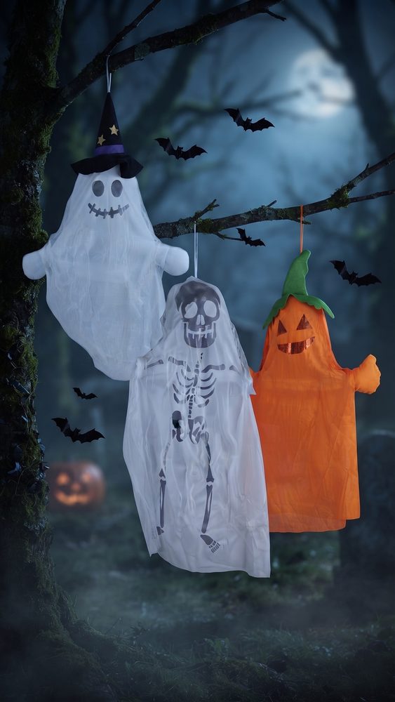 Drie Halloween hangdecoraties, een spook met heksenhoed, een skelet-spook en een pompoen, aan een boomtak